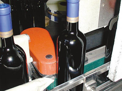 As wine bottles emerge from the heat tunnel that shrinks the capsule around the bottle neck, a vertical conveyor belt rotates th