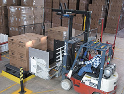 After delivering a load of boxed coolers onto the left side of the shuttle table, a clamp truck driver backs away and pulls a la