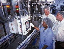 Set-up cartons convey in two lanes (above and inset) from left to right past a control panel toward the auger filling system (a