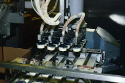 On the 2-oz line, the robotic head prepares to place 20 cups into a waiting case. To the left of the head is a sheet inserter th