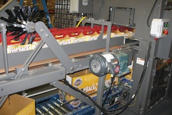 THE STUFFER. Freshly erected corrugated cases convey directly beneath empty paperboard six-pack carriers so the carriers can be inserted into the cases.