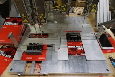 A black elastic staple is applied to a backing card to hold a hand exerciser in place.