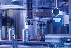 Closeup of labeler shows one can with a freshly cut label that has just been applied while the next can waits for application of its label.