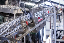 Closeup of labeler shows one can with a freshly cut label that has just been applied while the next can waits for application of its label.