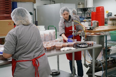 workers filling salsa into cups using piston filler