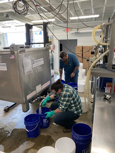 Kurt Justice (front) and David (Crash) Elliot (back) of Cardinal Spirits fill 5-gallon buckets of hand sanitizer that are being donated to emergency services like police and fire departments across Indiana.