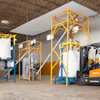 The flexible screw conveyor at left transfers roasted coffee beans from the bulk bag discharger to the grinder, while the conveyor at right moves ground coffee to the bulk bag filler.