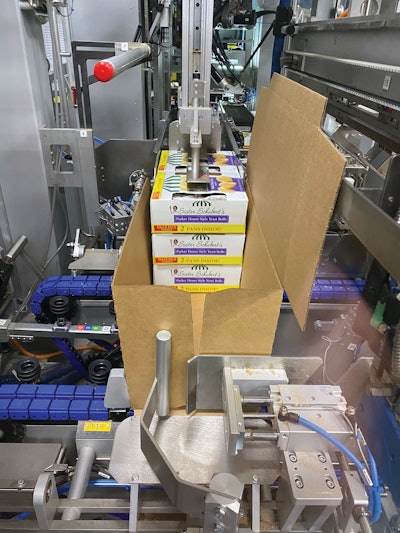 Six cartons in two stacks of three are pushed into the loading station of the wraparound case packer. Then the case is pushed at a right angle beneath folding bars and tooling that closes around the top to compress the top flap shut.