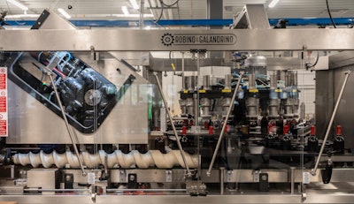 Bottles closed with corks have plastic laminated capsules applied by this machine.