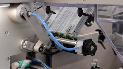 Literature or pamphlets are pulled from a magazine (upper right), then using belts, are shot (lower left corner) to a position between the tubes and the erected cartons. When a pusher pushed the tube into the carton, the pamphlet comes along for the ride, enveloping the tube entirely within the carton.