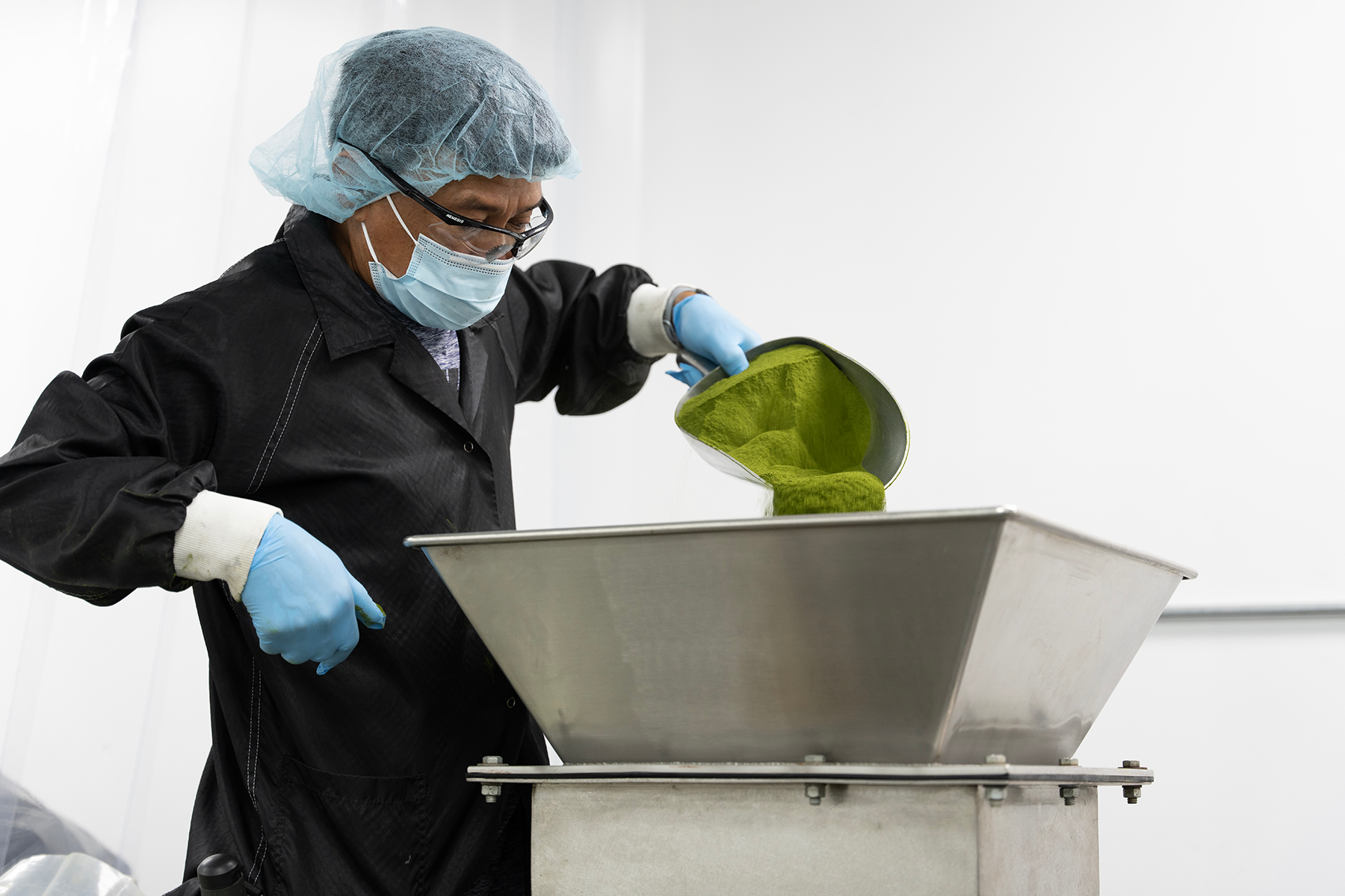 An operator empties a scoop of hand-weighed powder into the mixer intake, which remains stationary as the vessel turns.