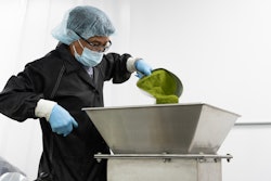 An operator empties a scoop of hand-weighed powder into the mixer intake, which remains stationary as the vessel turns.