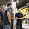 Industrial workers examining machinery near a yellow robotic arm in manufacturing facility