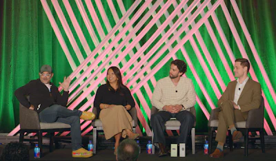 Four panelists seated on stage during a discussion in front of geometric pink and green backdrop
