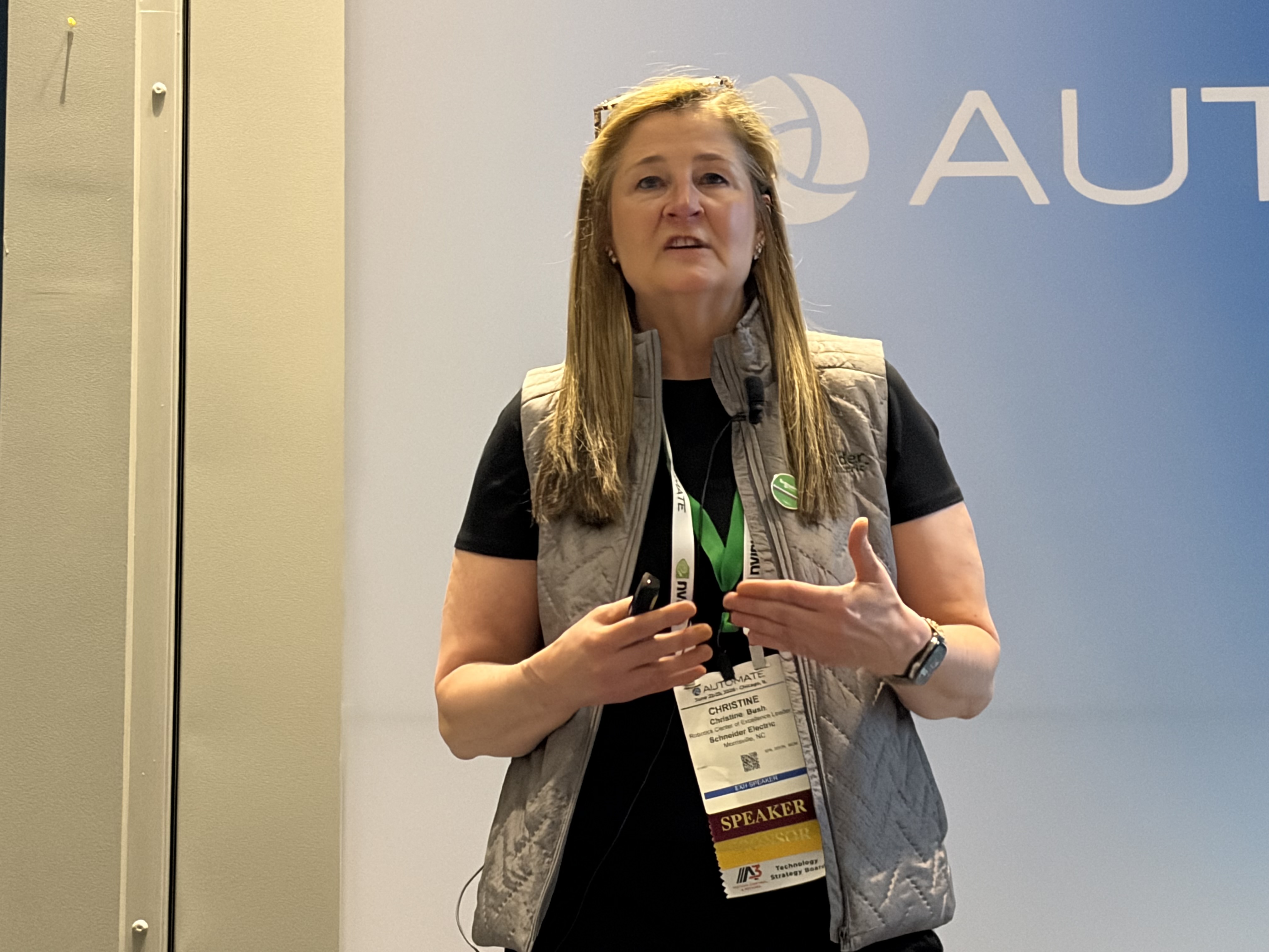 Woman speaker wearing lanyard badge presenting at conference with partial AUT logo visible in background