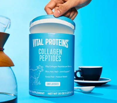Vital Proteins Collagen Peptides powder container with 20g collagen per serving, unflavored, held against blue background with coffee cup
