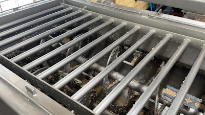 Industrial metal compartment with parallel dividers containing accumulated sediment and debris
