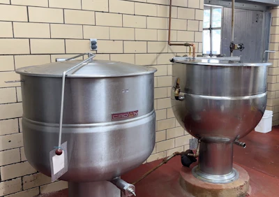 Industrial stainless steel brewing tanks with piping in a commercial kitchen facility