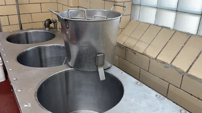 Commercial kitchen setup with large stainless steel pots and kettles mounted on counter with brick wall backdrop
