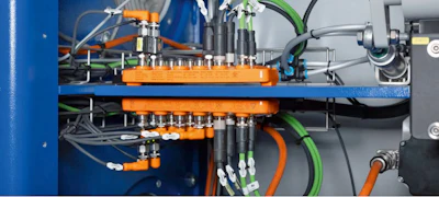 Industrial manifold assembly with orange valve blocks, green and orange tubing, and pneumatic connectors on blue mounting frame