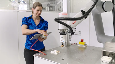 Woman in blue shirt operating ABB industrial robotic arm in laboratory setting with equipment on workbench