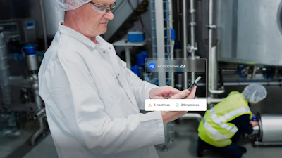 Factory worker in safety gear viewing machine management interface on tablet in industrial facility