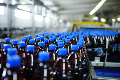 Factory production line with rows of brown glass bottles capped with blue lids in an industrial facility