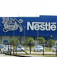 Nestlé manufacturing facility with blue facade, company logo, and parked vehicles in front