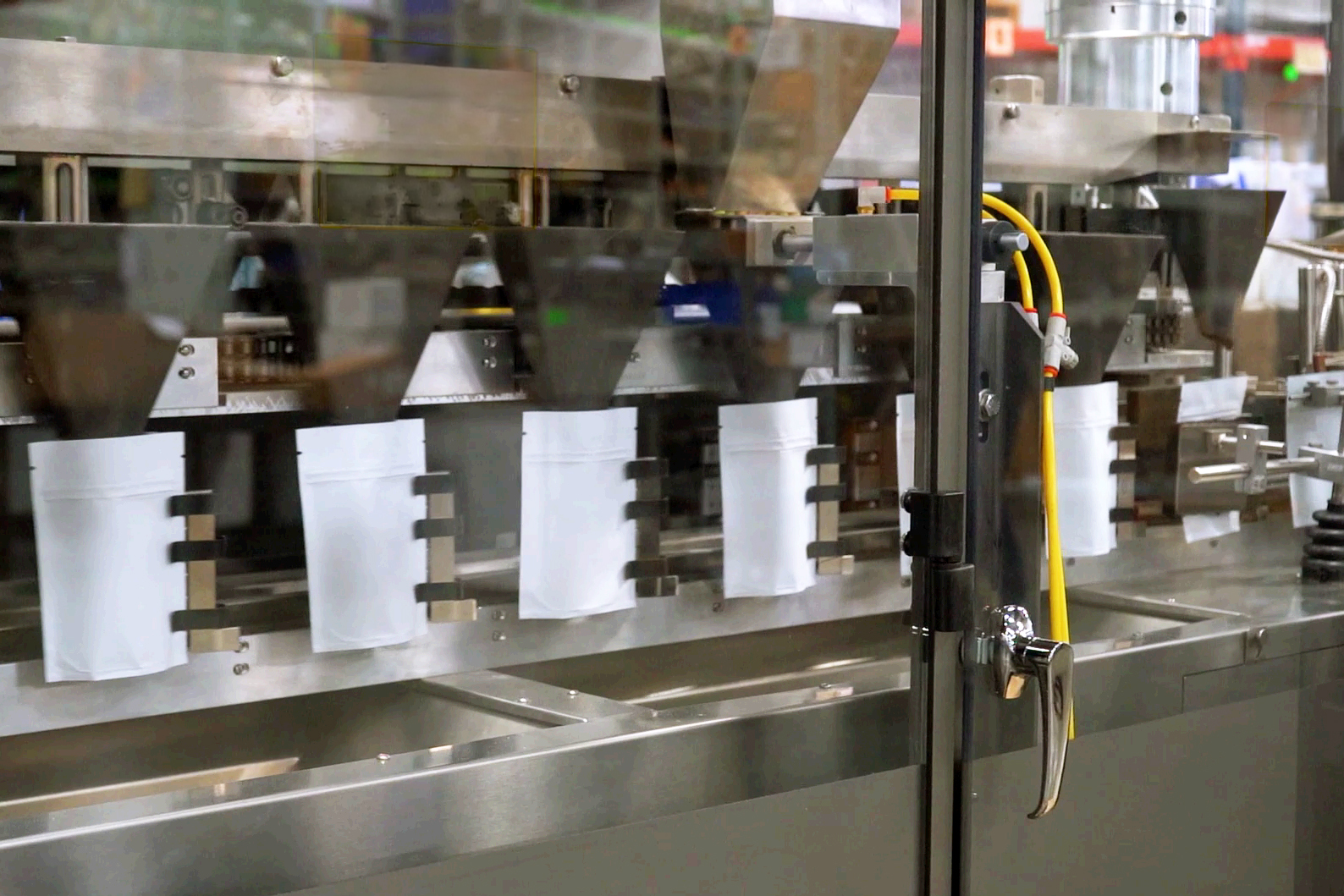 Industrial production line with white containers and metal equipment visible through glass enclosure