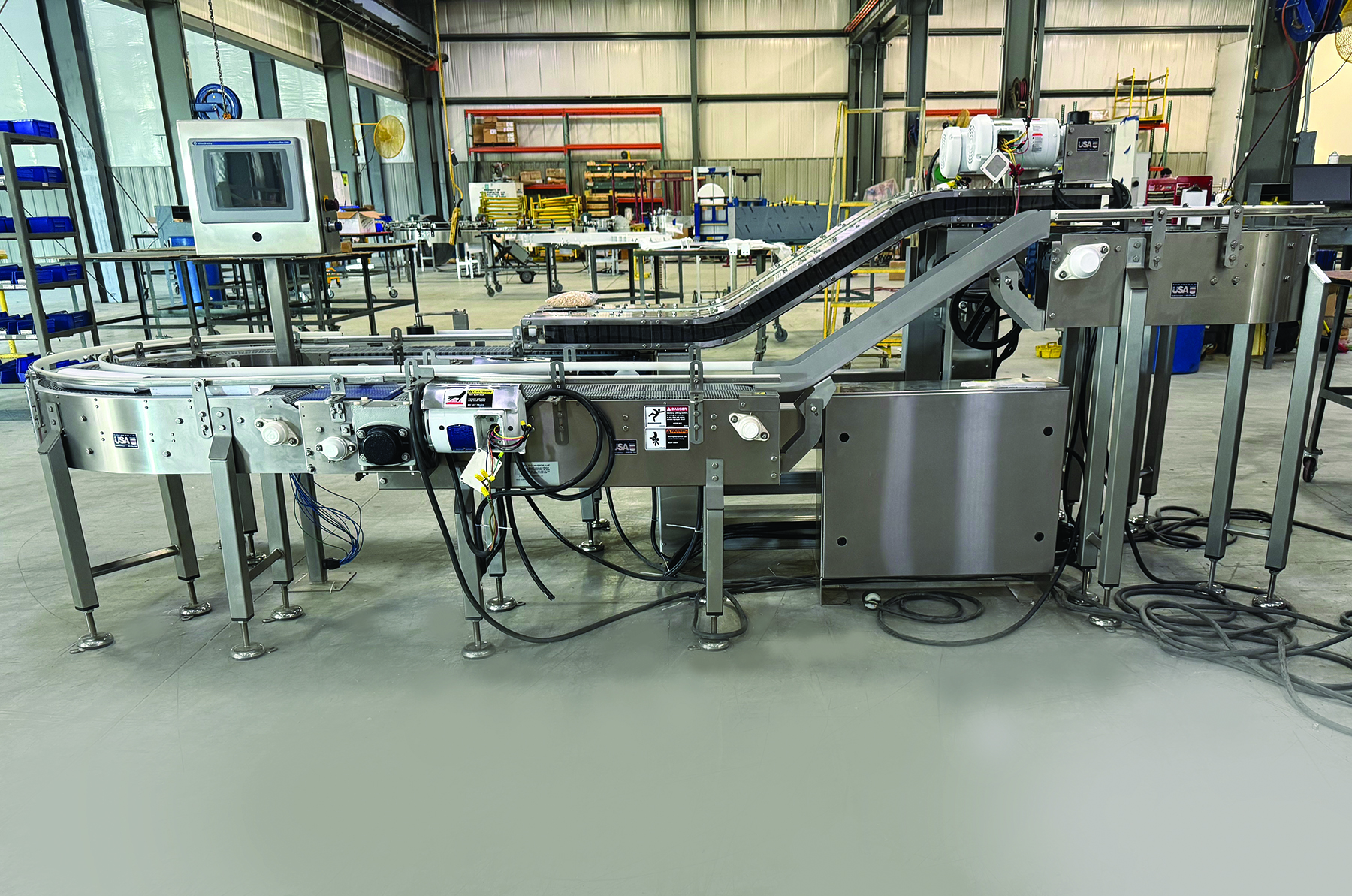 Industrial food processing equipment with conveyor systems and stainless steel machinery in a manufacturing facility warehouse.