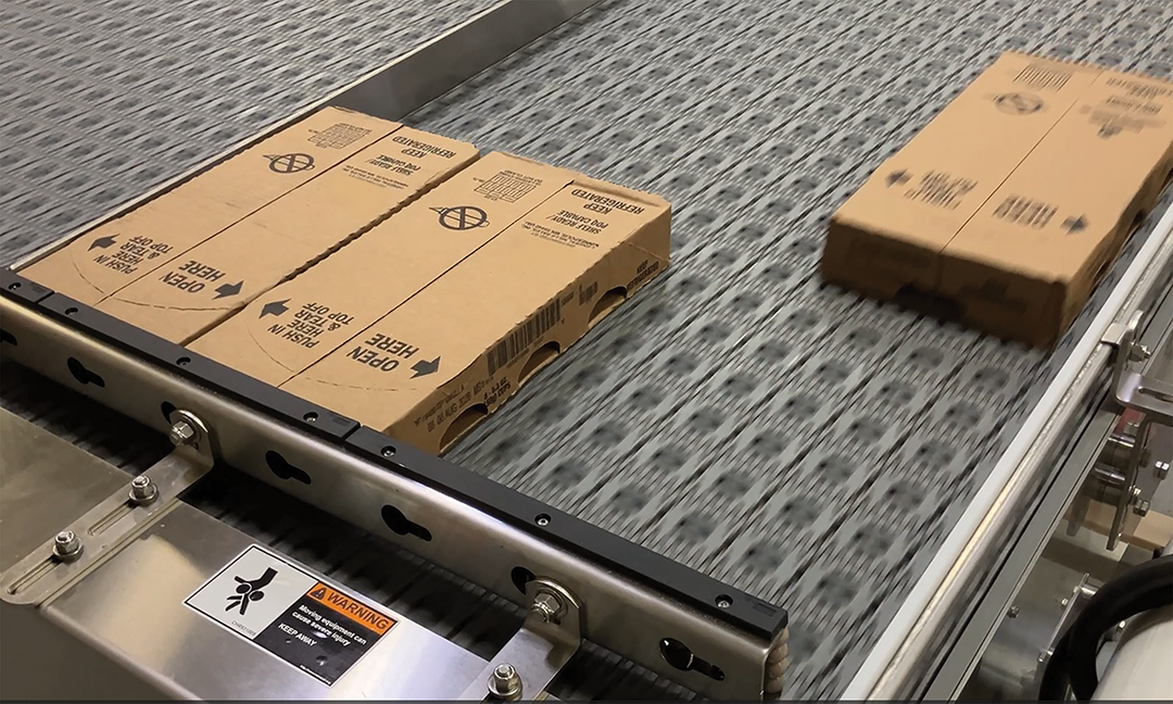 Cardboard shipping boxes on industrial conveyor belt with metal frame and gray textured surface
