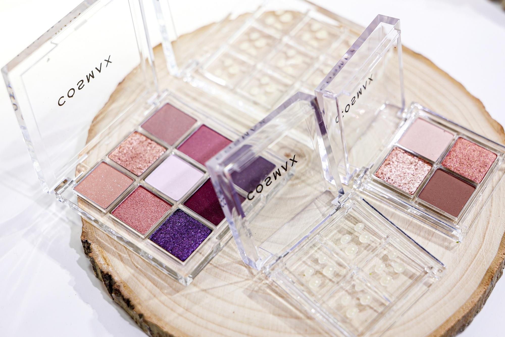 Coeunx eyeshadow palettes featuring multi-colored shimmer and matte shades in pink, purple, and gold tones displayed on textured surface