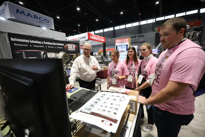 Team members in pink shirts demonstrate automated labeling equipment at MARCO trade show booth