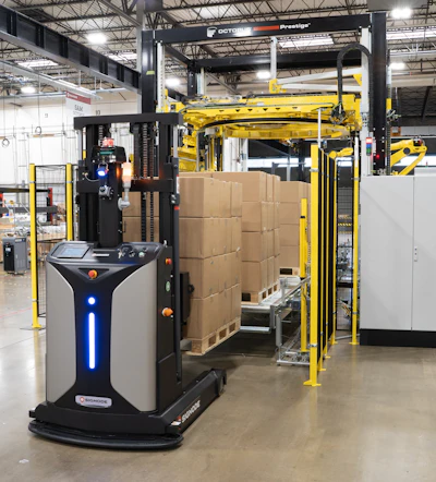 Automated guided vehicle with yellow gantry system handling cardboard boxes in industrial warehouse facility