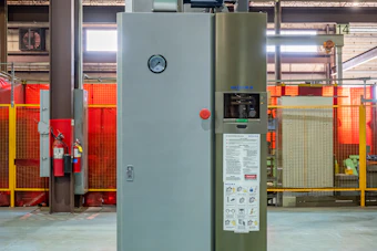 Industrial furnace or oven system with gray and olive-green panels in a warehouse facility with red safety barriers