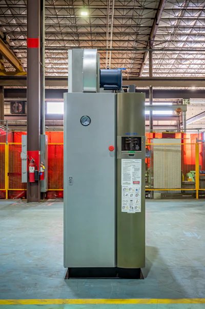 Industrial furnace or oven system with gray and olive-green panels in a warehouse facility with red safety barriers