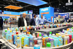 Three professionals examine colorful consumer product bottles displayed on curved tables at a trade show booth with blue and orange Bpda branding.