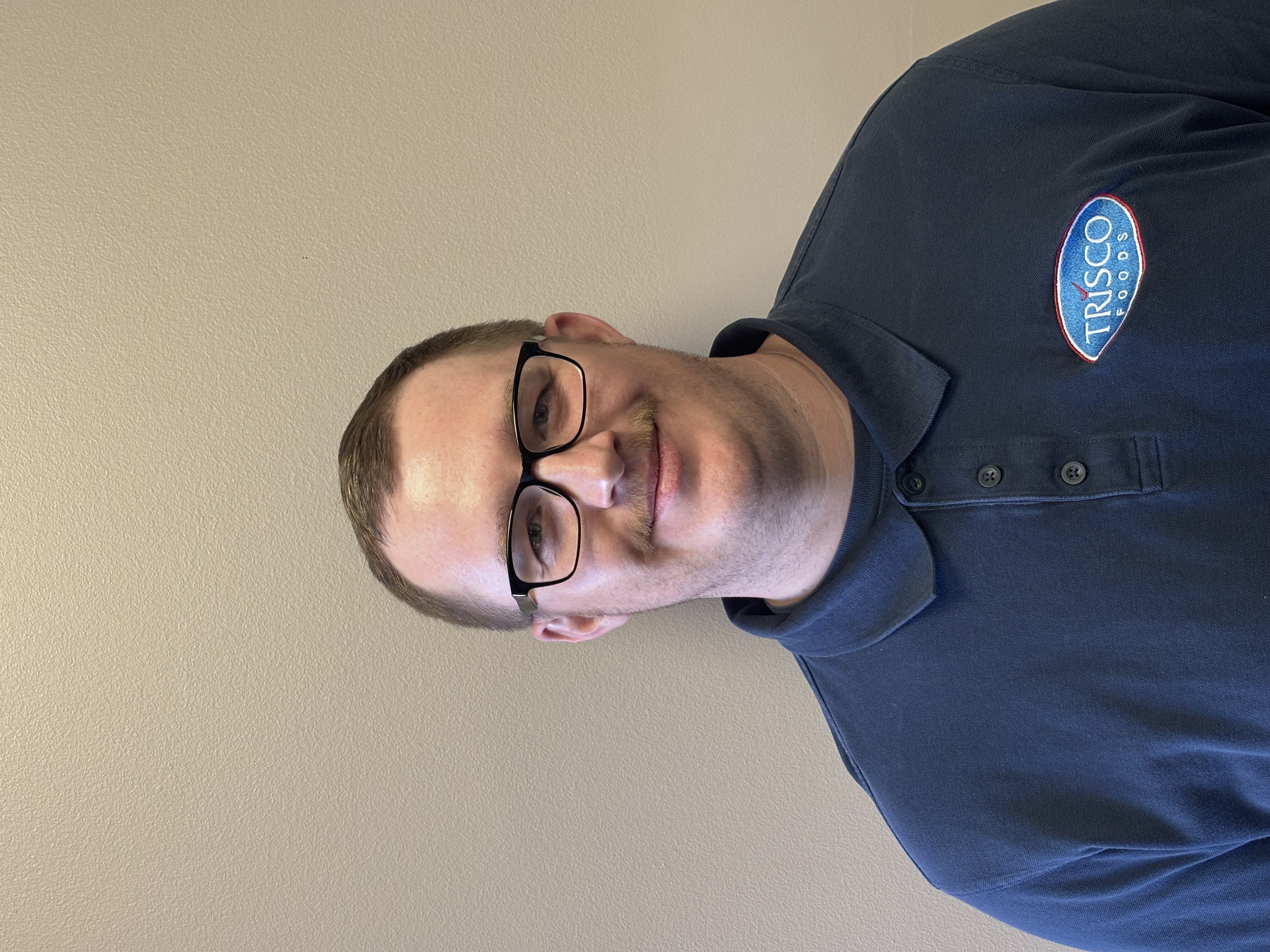 Professional headshot of man wearing navy Trisco Foods polo shirt with glasses against neutral background