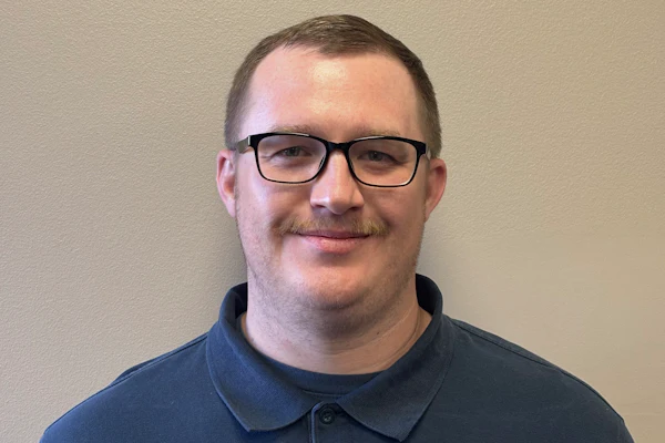 Professional headshot of man wearing navy Trisco Foods polo shirt with glasses against neutral background