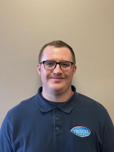 Professional headshot of man wearing navy Trisco Foods polo shirt with glasses against neutral background
