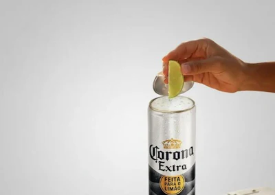Hand squeezing lime into Corona Extra beer bottle on white background