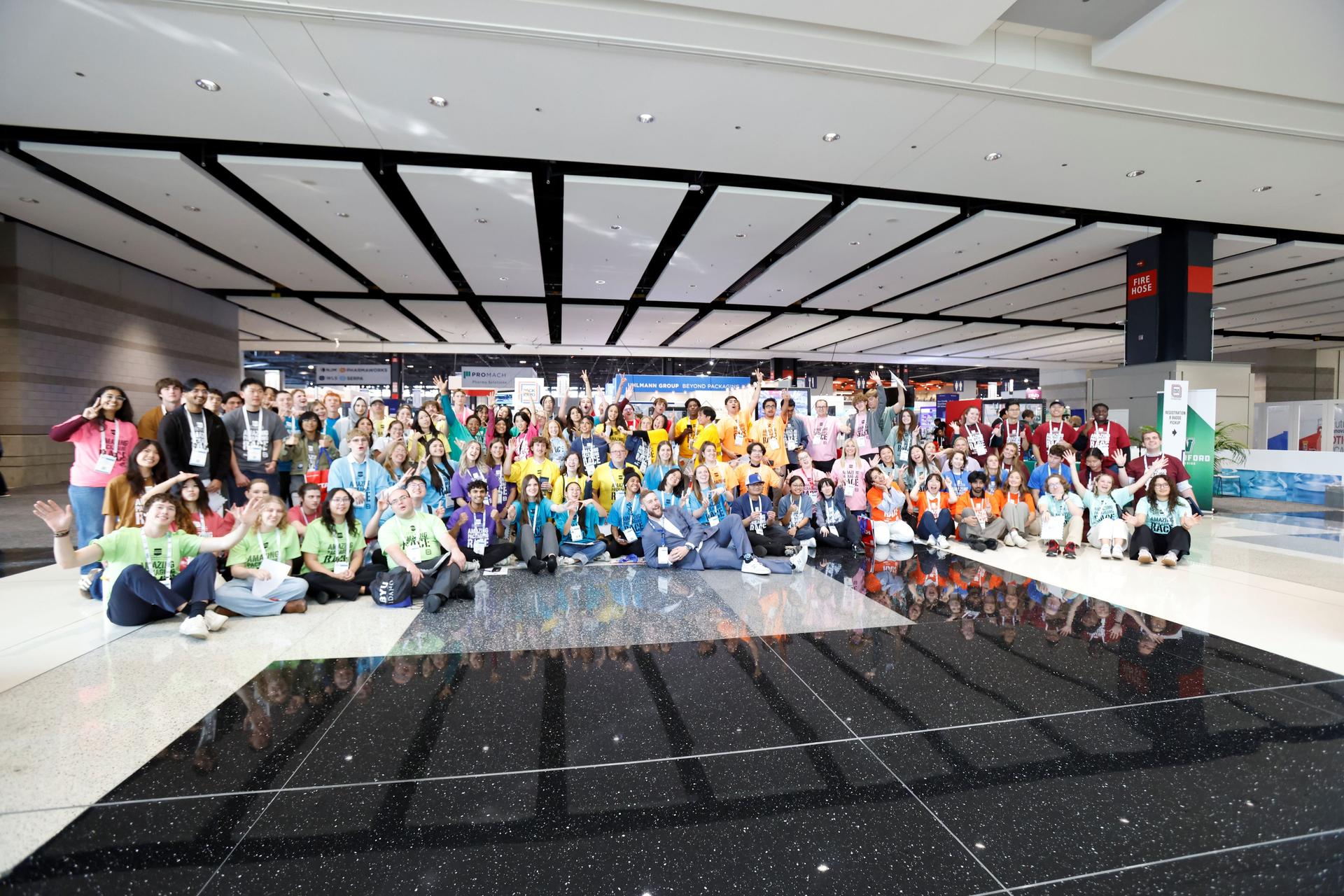 Large diverse group of people posing together in a modern convention center or conference venue with geometric ceiling design.