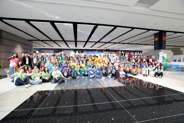 Large diverse group of people posing together in a modern convention center or conference venue with geometric ceiling design.