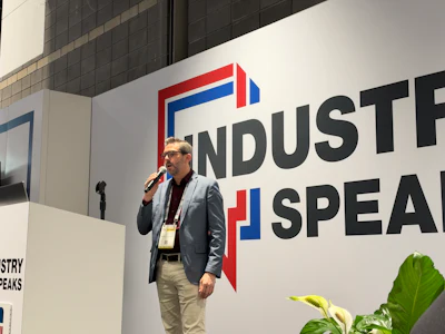 Professional speaker presenting at Industry Speaks conference podium with branded wall backdrop