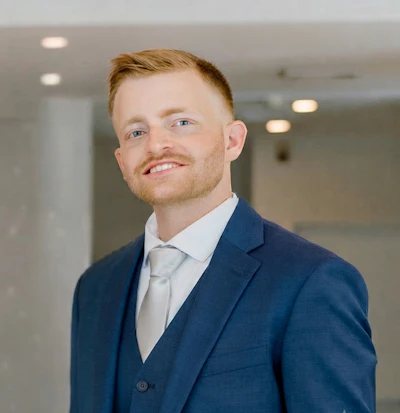 Professional man in navy blazer and gray tie smiling at camera in modern office setting