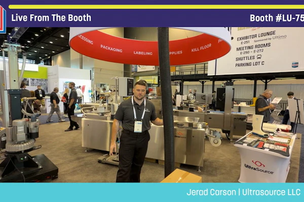 Professional at Pack Expo booth #LU-7503 demonstrating packaging equipment under red umbrella display