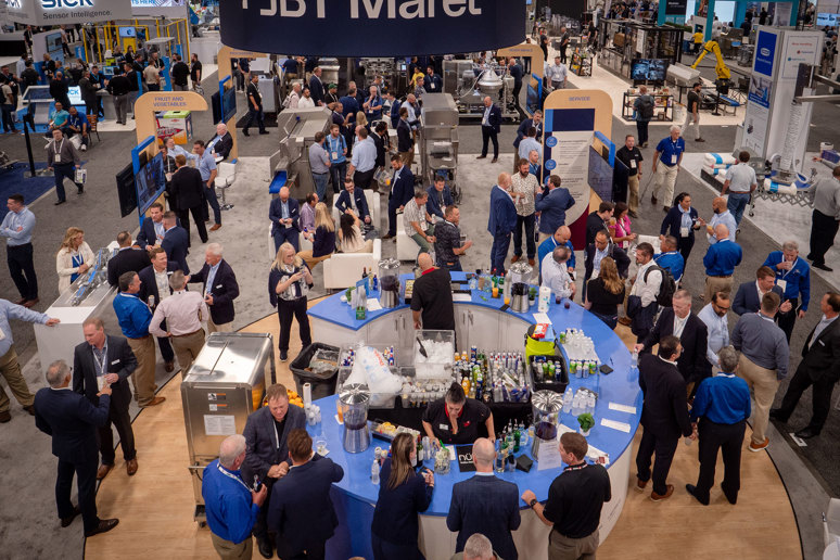 Overhead view of crowded trade show floor with blue booth tables, attendees in business attire, and exhibition signage