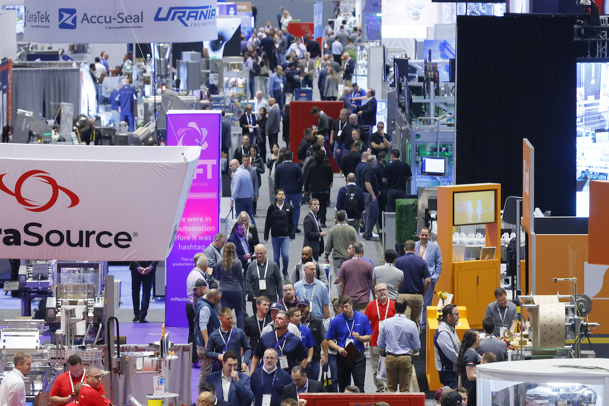 Busy trade show exhibition floor with multiple vendor booths, attendees in business attire, and corporate signage including DataSource, Accu-Seal, and Urani branding.