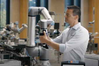 Engineer operating a white collaborative robotic arm in an industrial laboratory setting